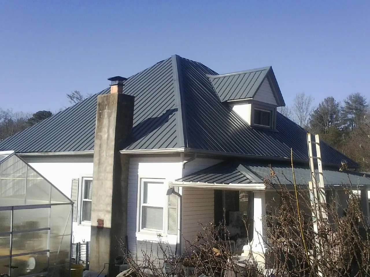 Dark blue standing seam metal roof on a white farmhouse with dormer — Slate & Tile Roof Repair by Roofing Brothers in Middle Village
