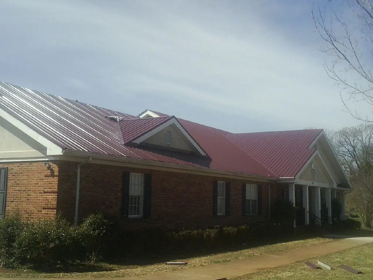 Red metal roof with gabled entries on a long brick building, from a Hail Damage Roof Repair job in Middle Village