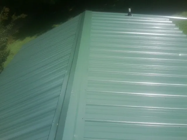 New green metal panels meeting at the ridge of a roof — Flat Roof Repair work by our crew in Middle Village