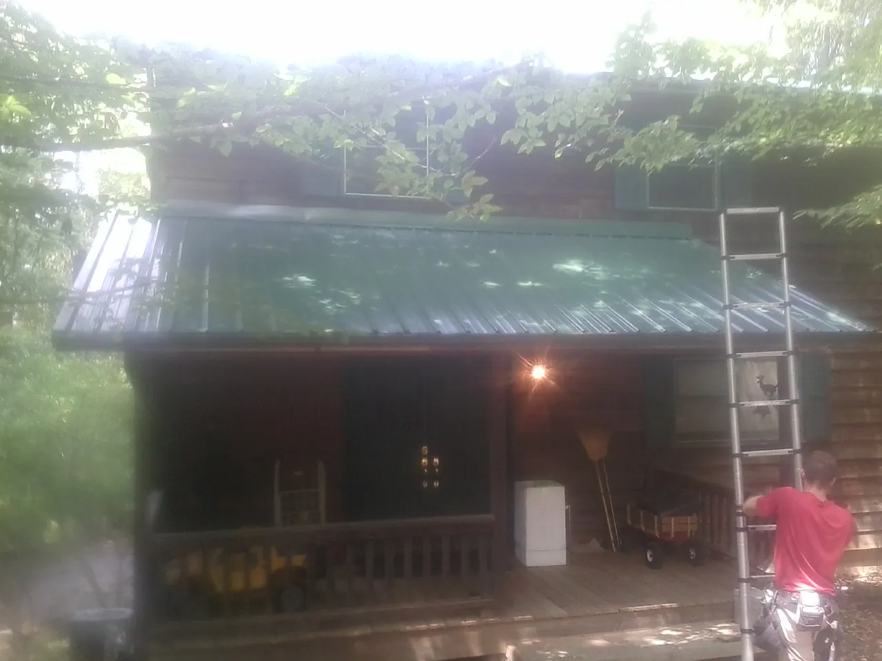 Worker on a ladder at the green porch roof of a wooded cabin in Middle Village