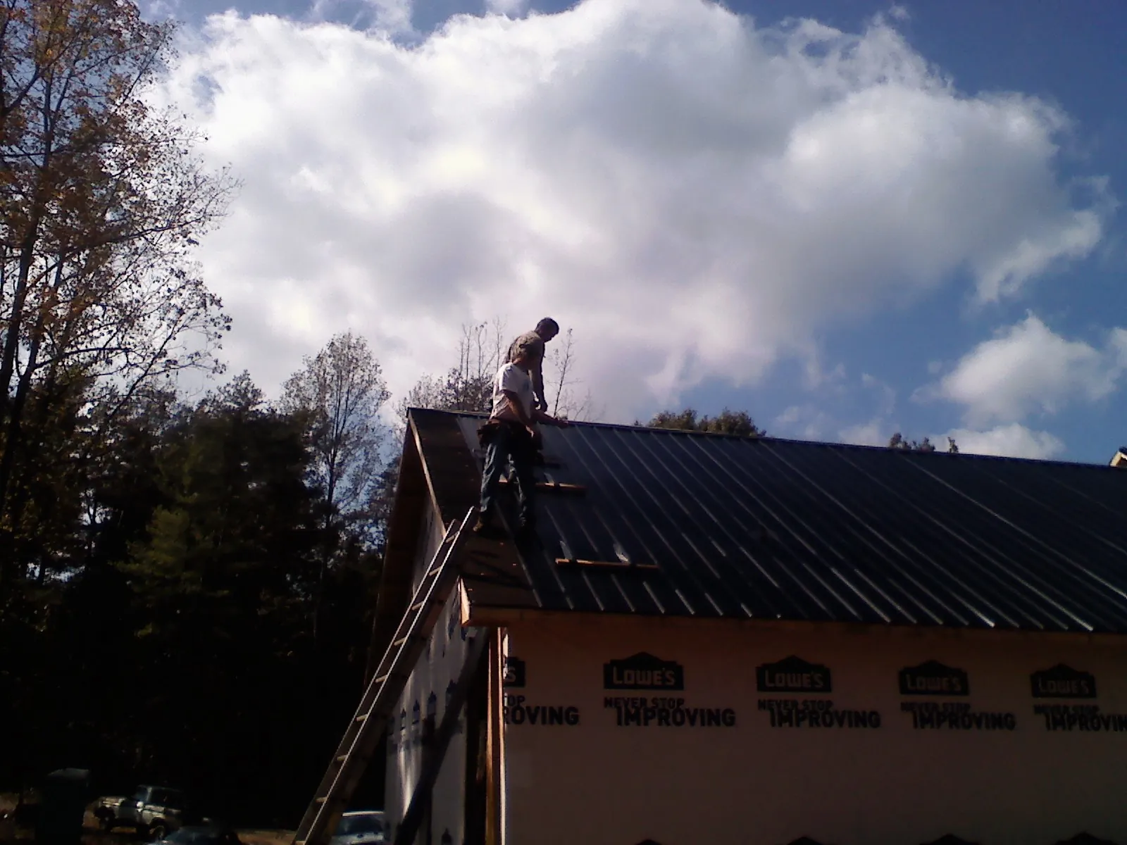 Roofer fastening dark metal panels high against a cloudy sky, from a Roof Inspection job in Middle Village