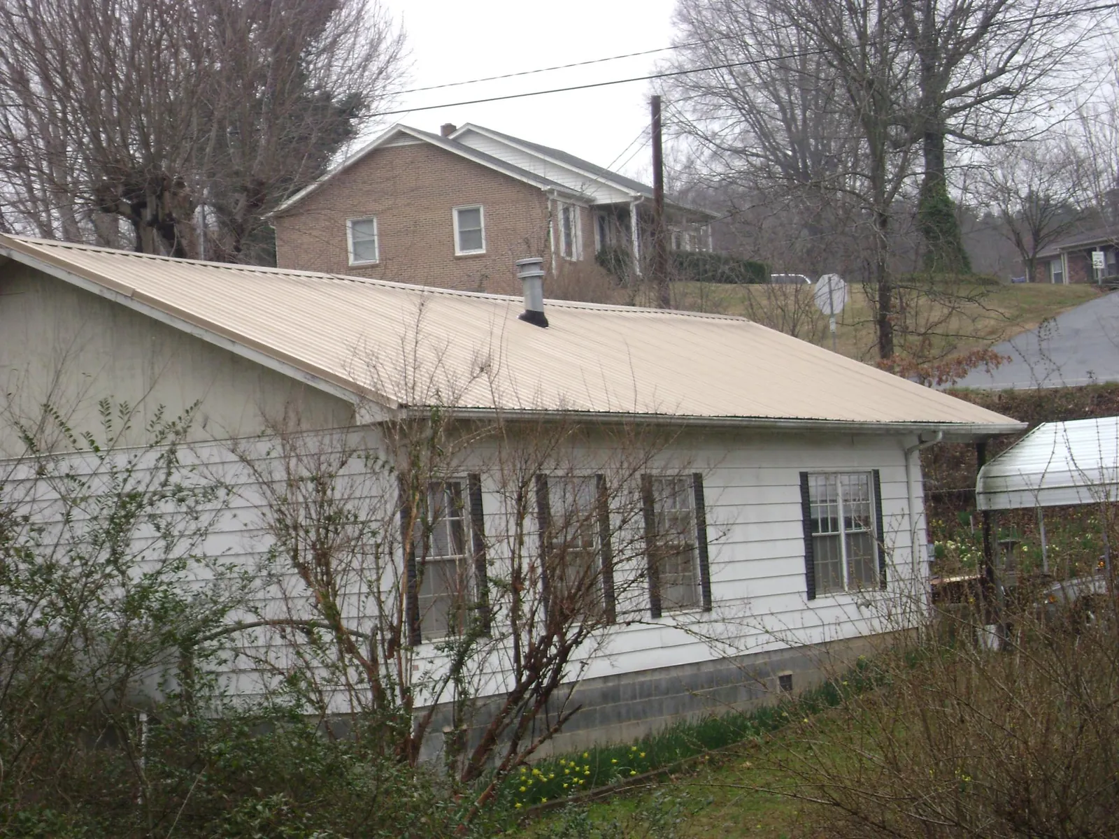 Tan metal roof on a white sided house set into a hillside — Commercial Roofing by Roofing Brothers in Middle Village