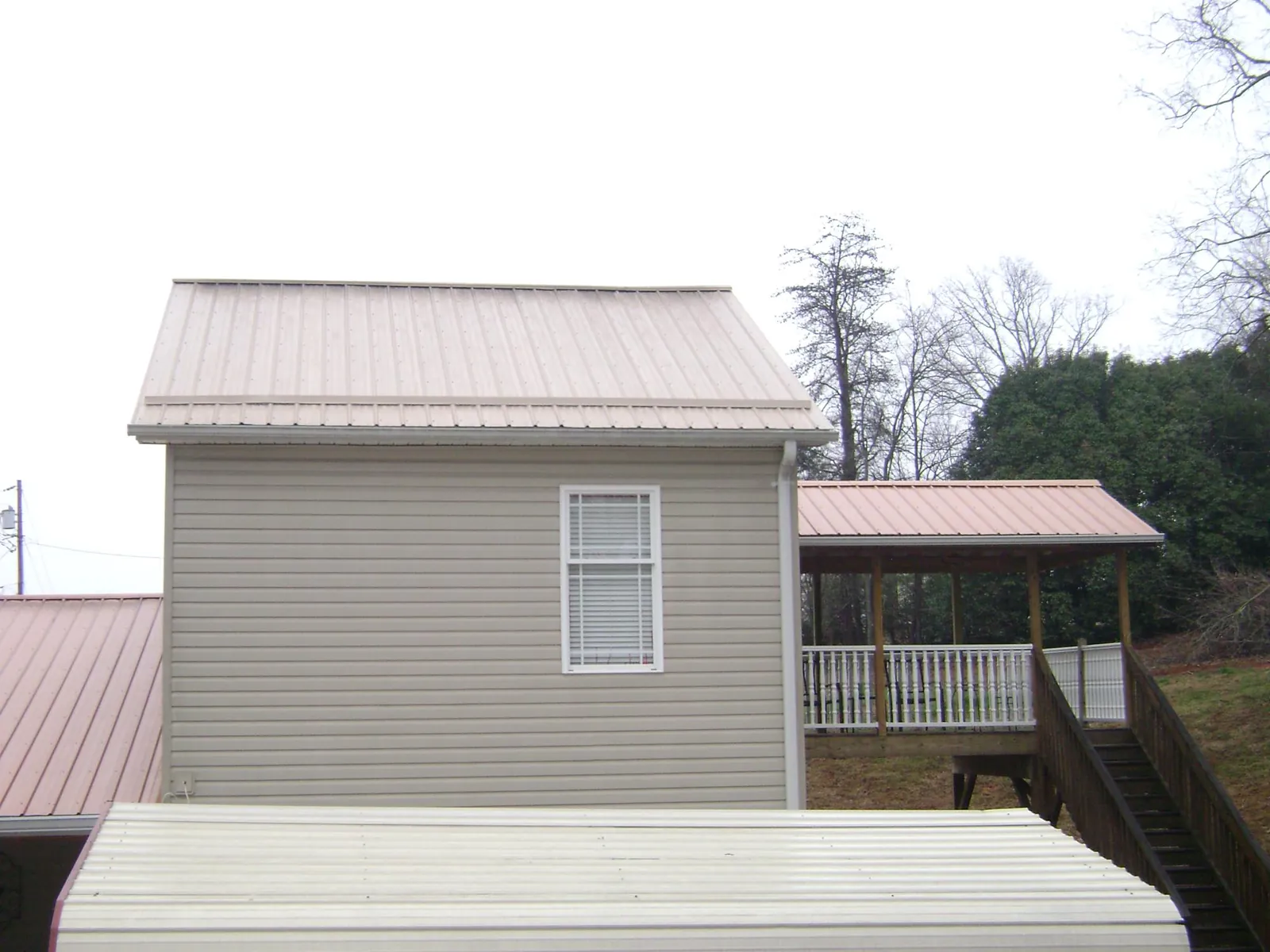 Tan metal roofs on a two story addition and attached porch, from a Roof Replacement job in Middle Village