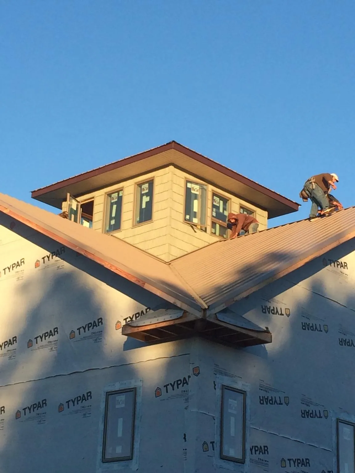 Roofers working around a rooftop cupola on a new metal roof at sunset — Roof Waterproofing in Middle Village by Roofing Brothers